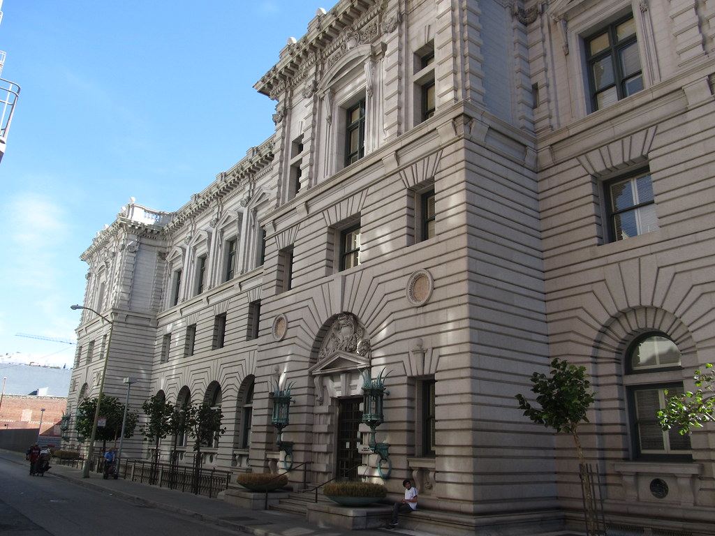 Ornate gray stone federal courthouse with arched windows and green lanterns beside a sunny street