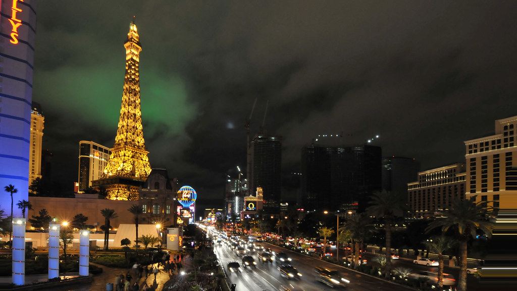 The Las Vegas Strip at night, with a lit Eiffel Tower replica, hotel towers and busy traffic on the boulevard