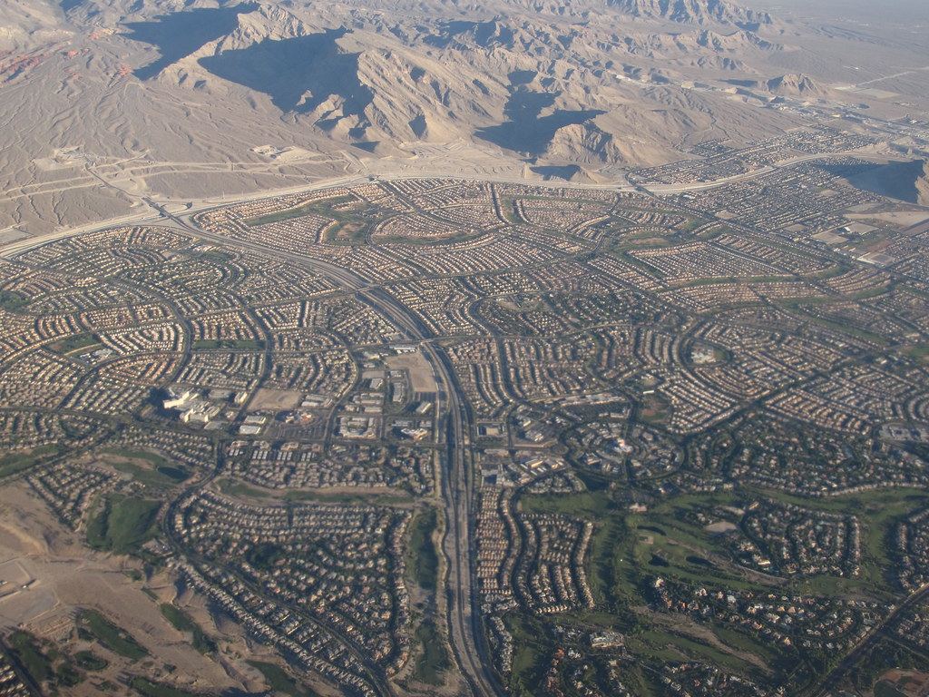Aerial view of sprawling suburban housing tracts and a highway at the foot of barren desert mountains