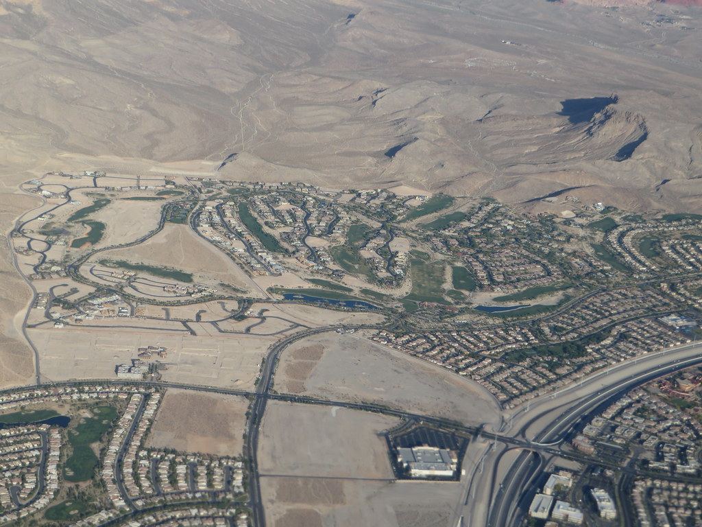 Aerial view of suburban housing developments, golf course greens and a freeway at the edge of desert mountains