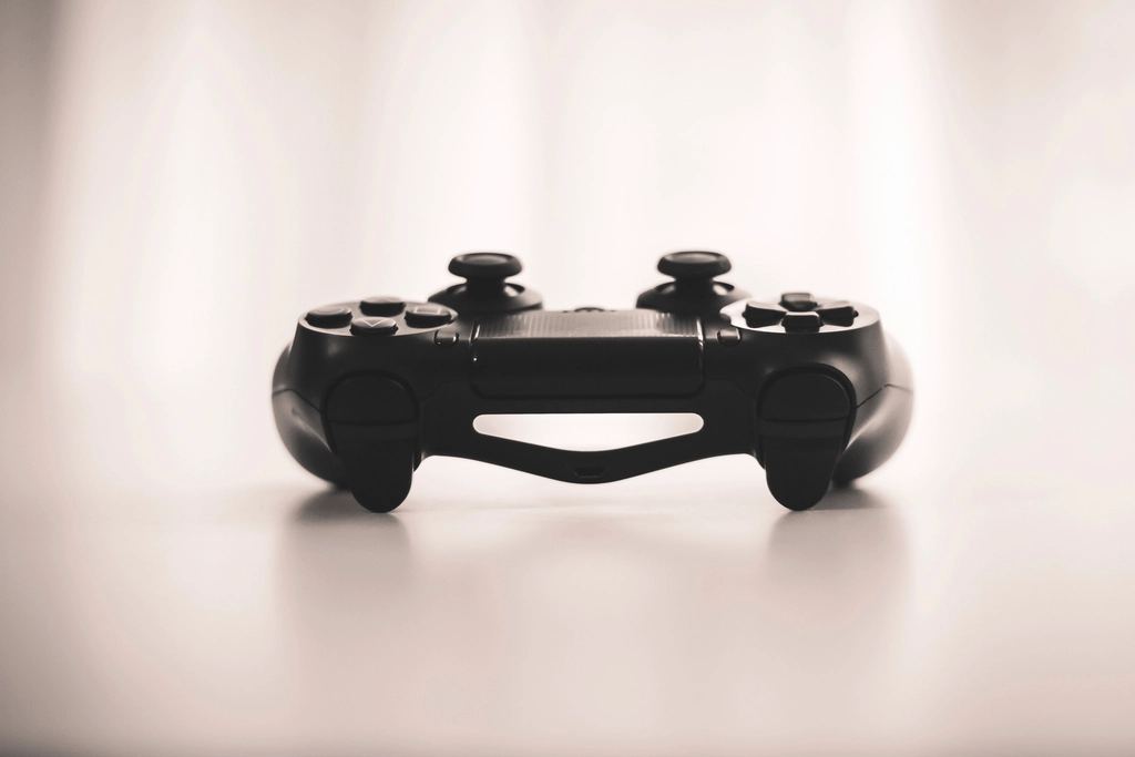 A black video game controller sitting on a pale, softly lit surface
