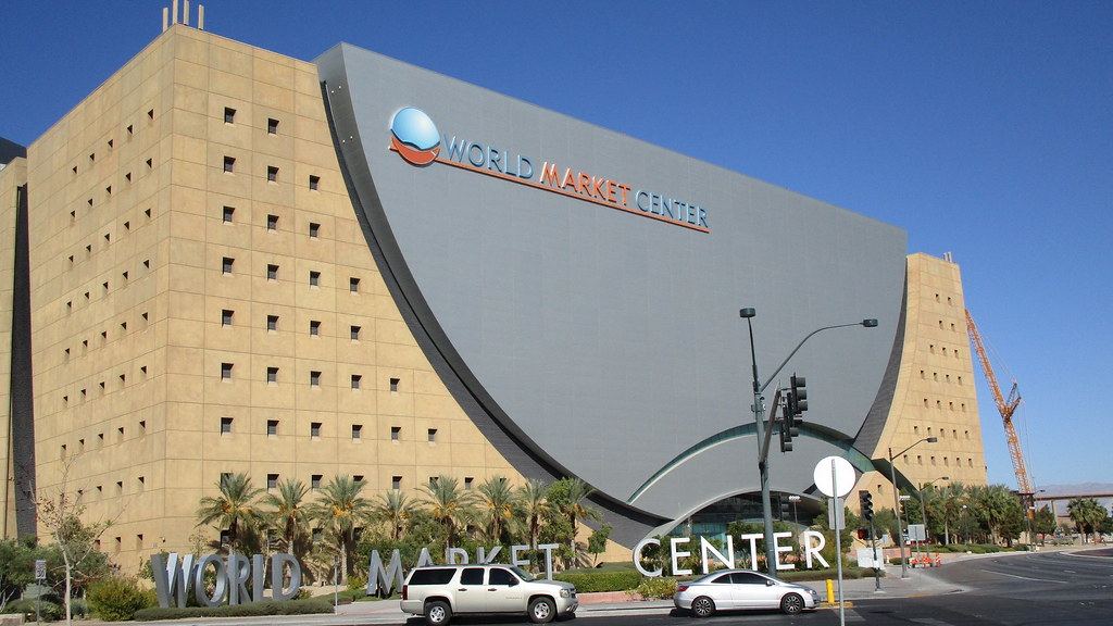 Large tan and gray World Market Center building with palm trees, street lights and cars under a clear blue sky