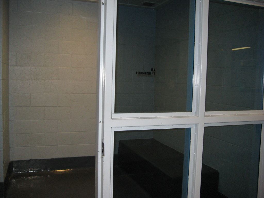A holding cell with cinder block walls, a bench and windowed white doors, marked Holding Cell #2