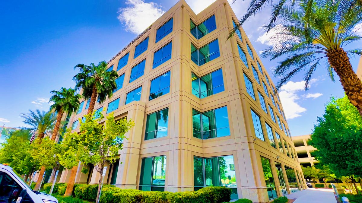 A beige multi-story office building with blue-tinted windows, surrounded by palm trees under a blue sky