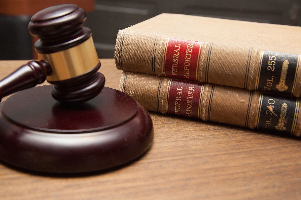 A wooden judge's gavel on its block beside two stacked Federal Reporter law books on a wooden desk
