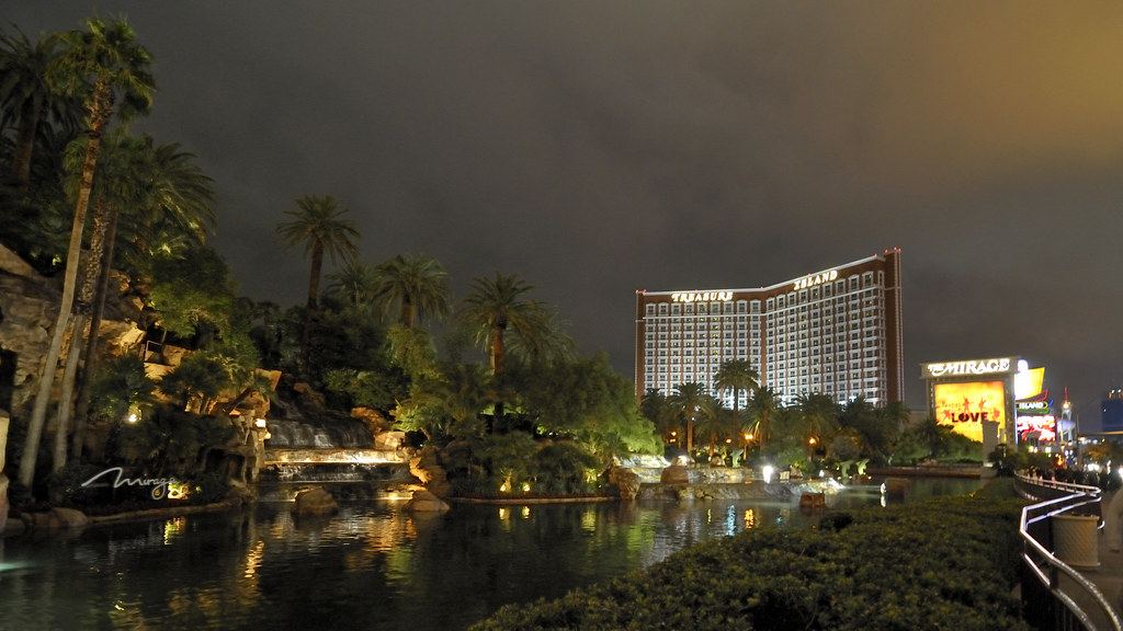Lagoon, palm trees and a lit hotel tower on the Las Vegas Strip at night under a dark, cloudy sky