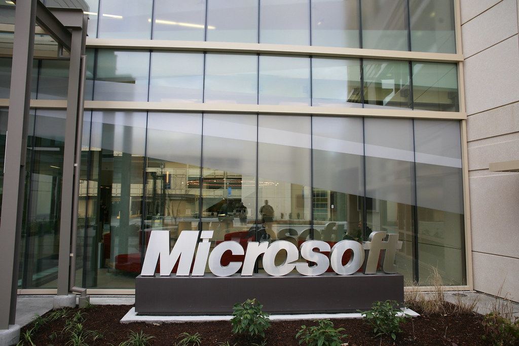 Large silver Microsoft letters on a sign in front of a glass-walled office building