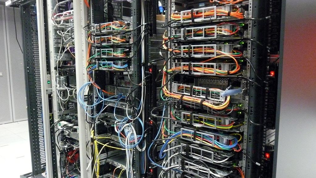 Rows of server racks with bundles of orange, blue, green and white network cables in a data center