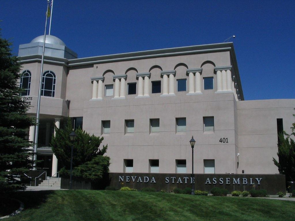 Beige legislative building with a silver dome and columns, with a 'Nevada State Assembly' sign on the lawn