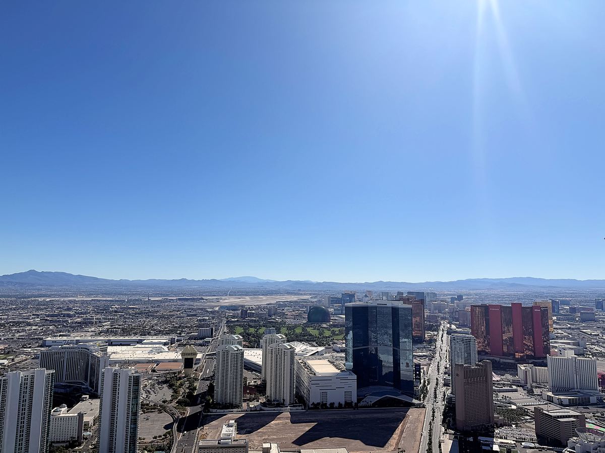 Aerial view of Las Vegas high-rise hotels and city sprawl under a clear blue sky, with mountains on the horizon