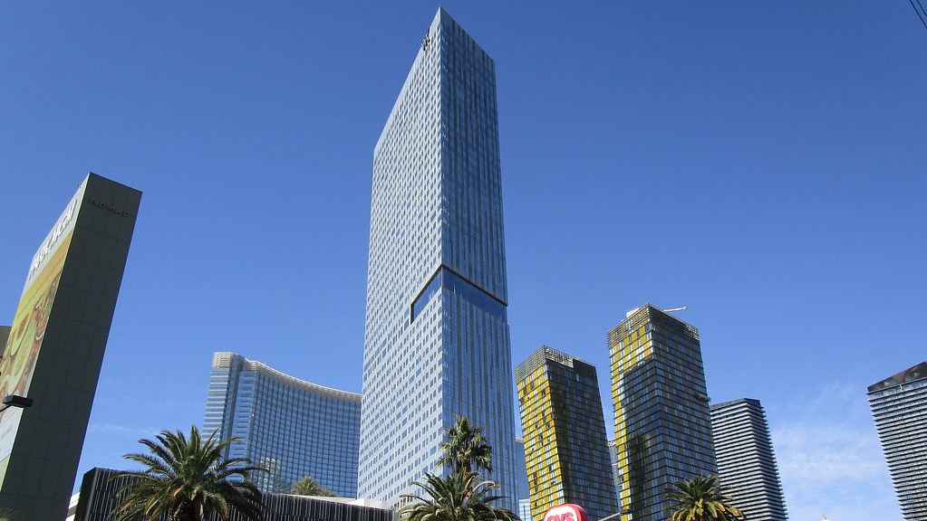 Glass high-rise hotel towers and palm trees along the Las Vegas Strip under a clear blue sky