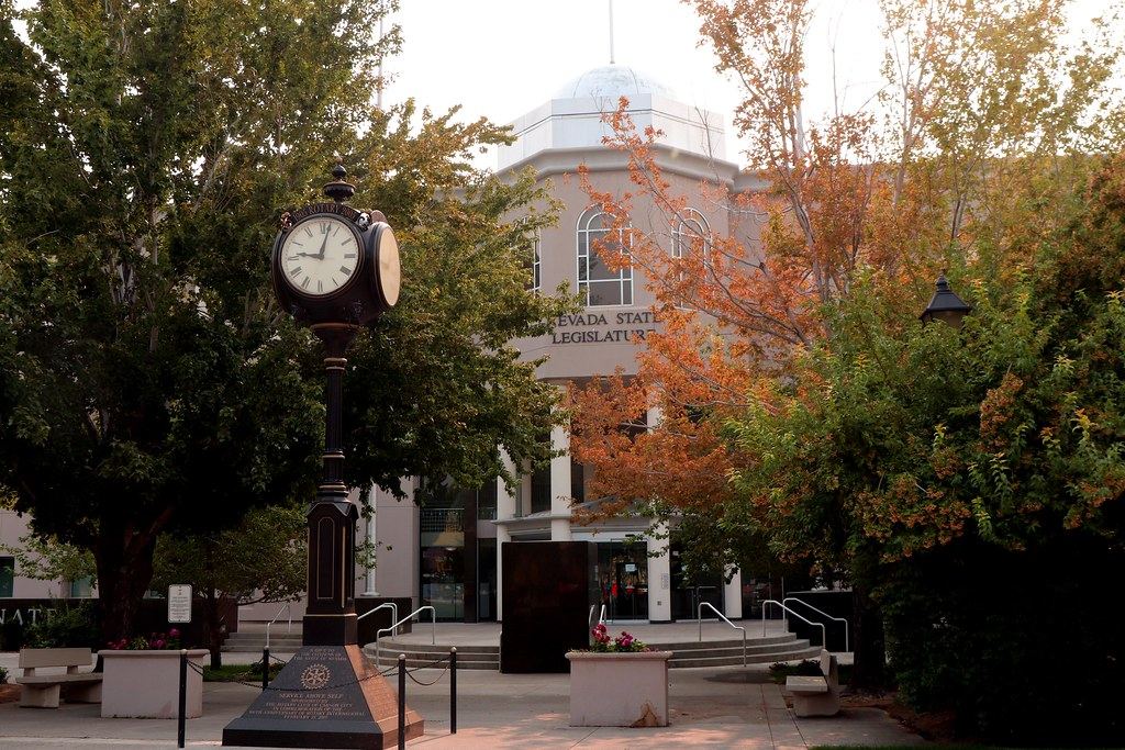 A street clock and autumn trees stand in front of the domed Nevada State Legislature building