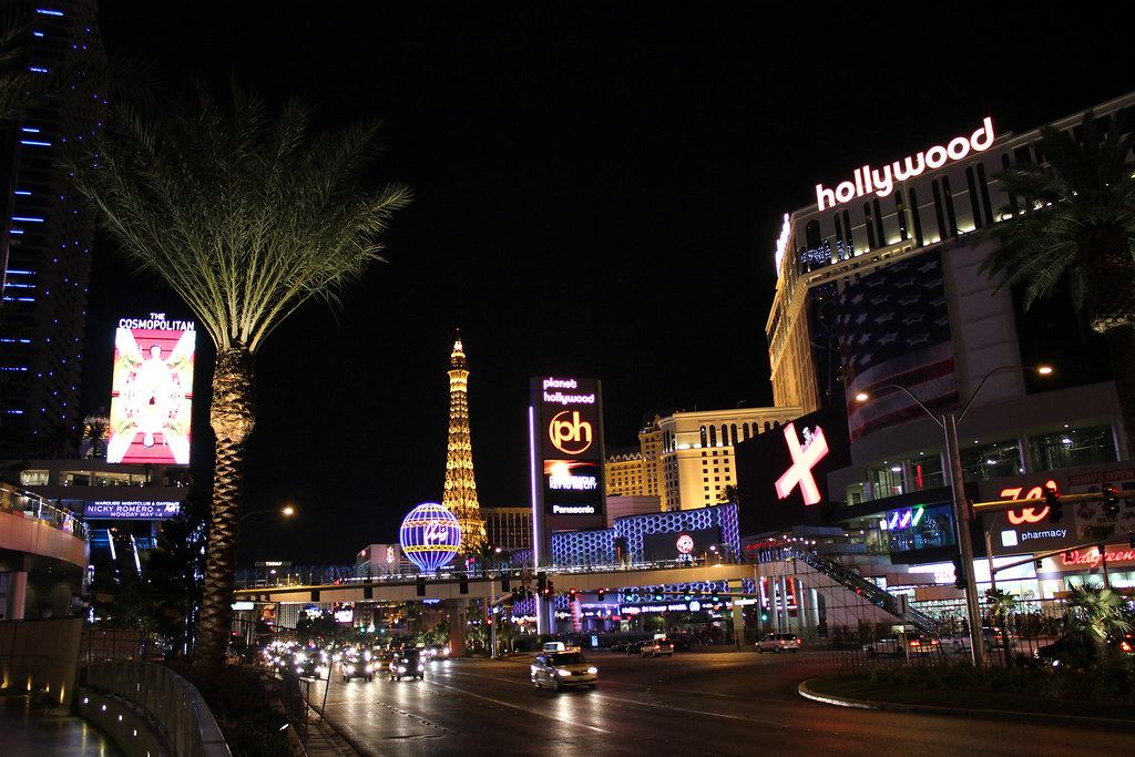 The Las Vegas Strip at night, with lit casino signs, a replica Eiffel Tower, palm trees and traffic