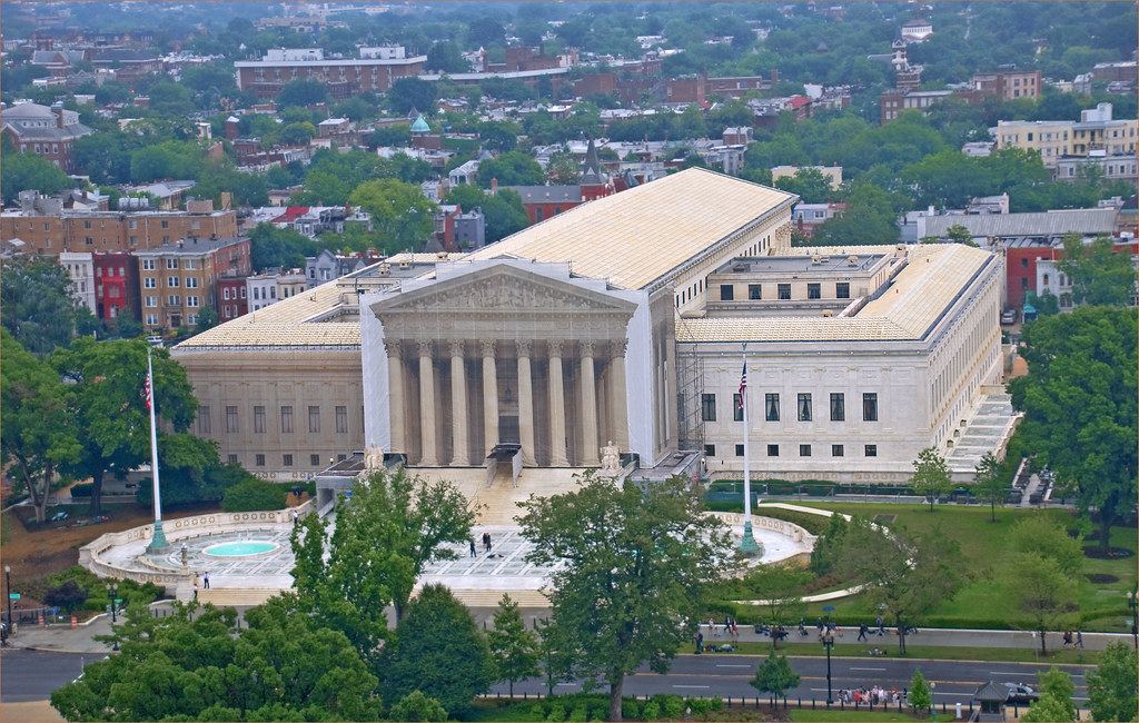 Aerial view of the U.S. Supreme Court building with partial scaffolding, surrounded by trees and city buildings