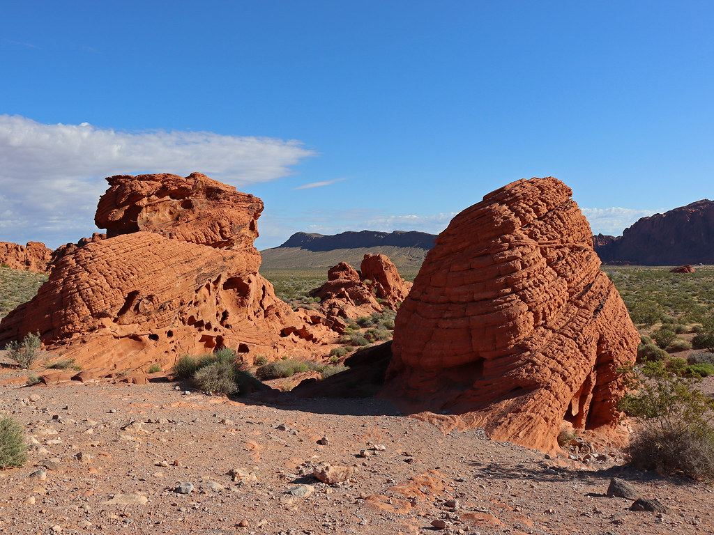 Two large red sandstone rock formations with layered, honeycomb texture stand in a desert under a blue sky