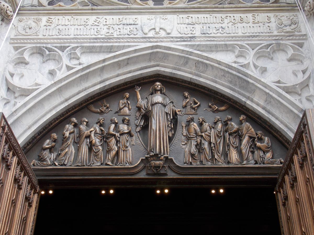 Bronze relief of Christ and apostles above a Gothic marble doorway with a carved Latin inscription