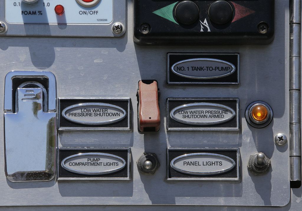 Close-up of a fire engine pump control panel with toggle switches, labeled plates and an amber indicator light
