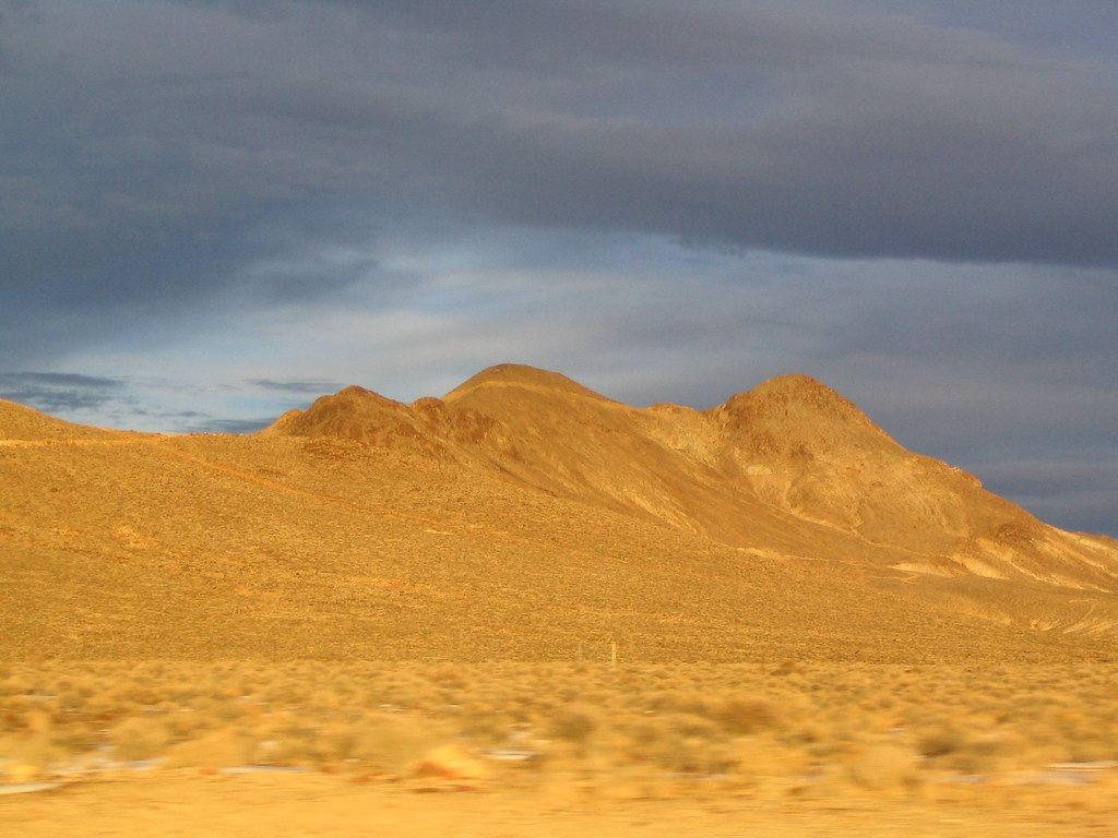 Sunlit desert hills covered in sagebrush beneath a cloudy gray-blue sky