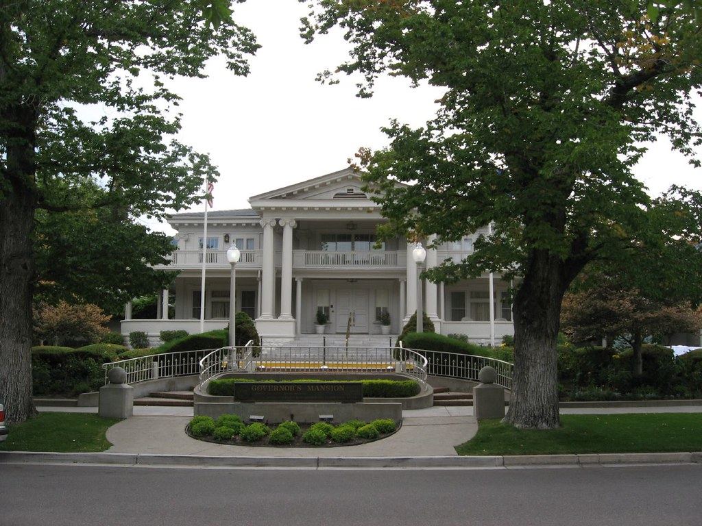White neoclassical mansion with columns and balconies behind trees, a 'Governor's Mansion' sign and landscaped entry