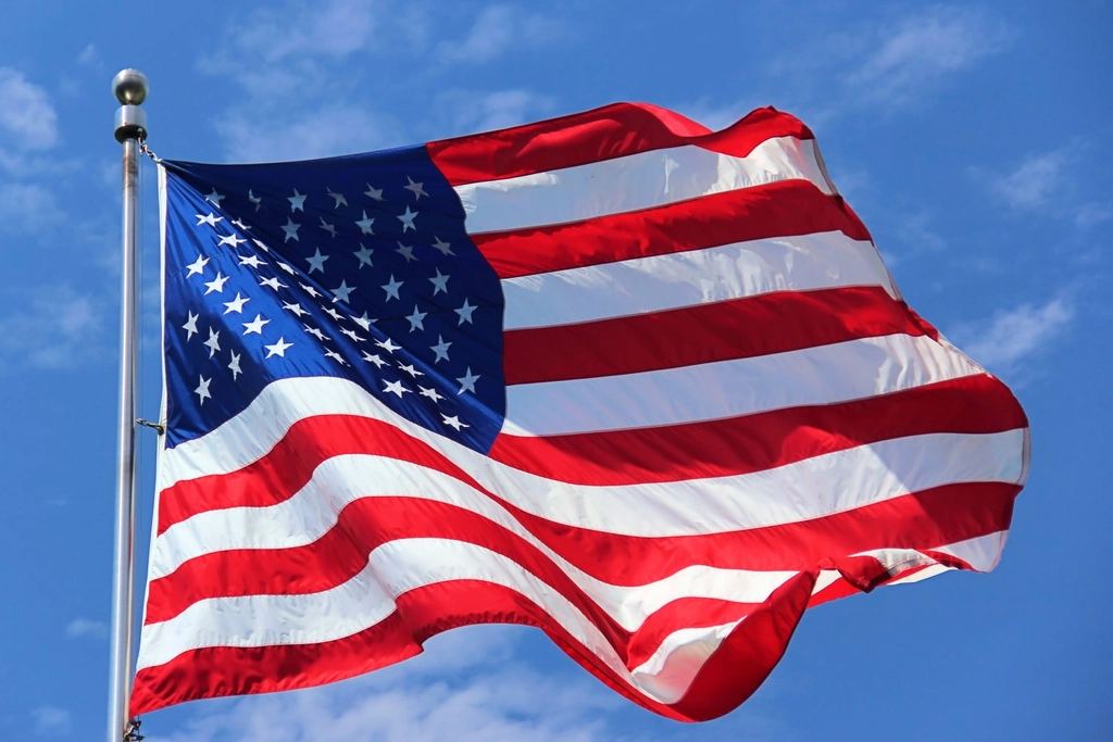 An American flag on a metal pole waves against a blue sky with light clouds