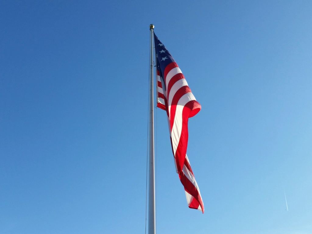 An American flag waves on a tall flagpole against a clear blue sky