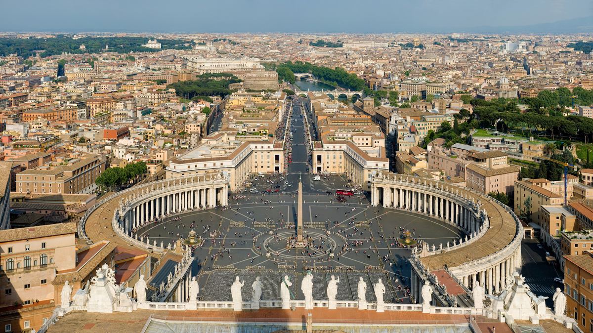 Aerial view of St. Peter's Square with its obelisk and curved colonnades, looking out over Rome