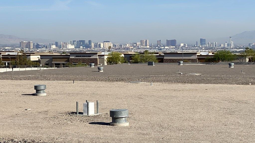 Distant view of the Las Vegas Strip skyline beyond a gravel field with vents and low buildings