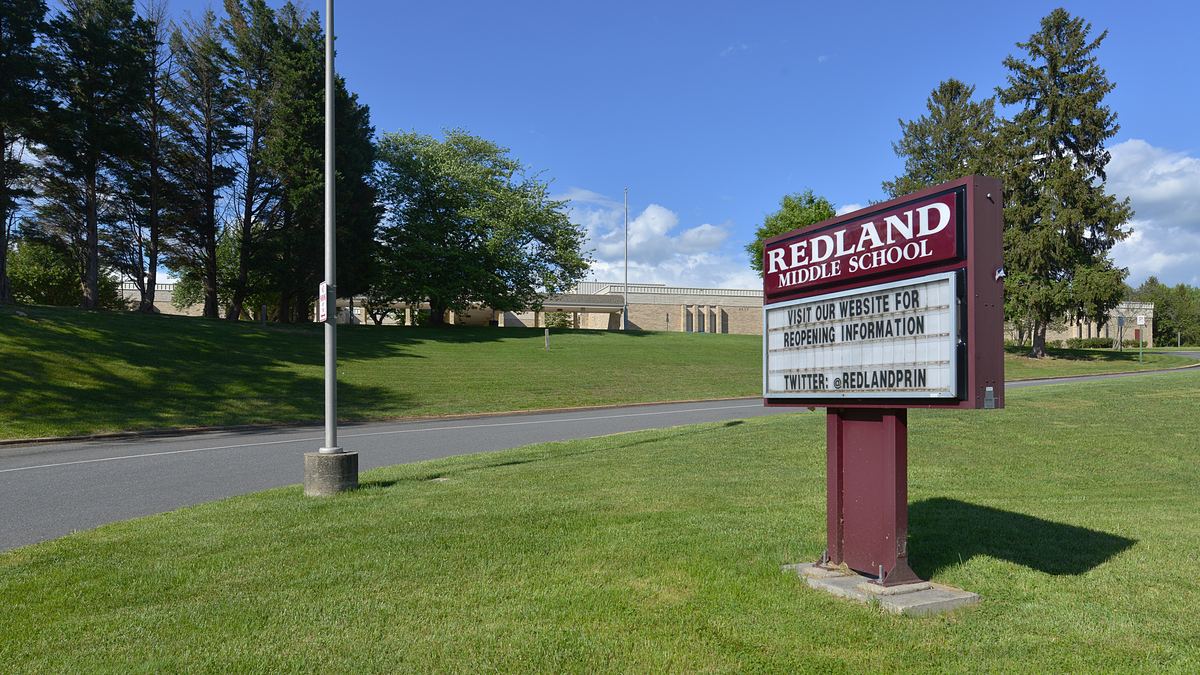 A maroon Redland Middle School sign on a grassy lawn beside a road, with the low school building behind trees