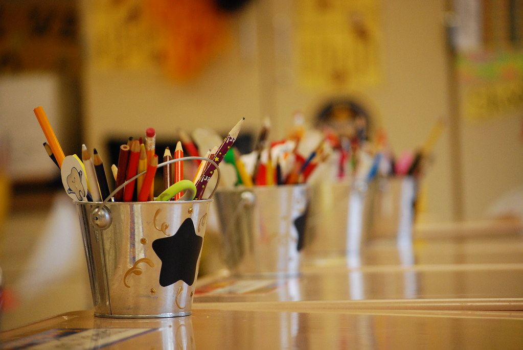 Metal buckets filled with pencils and colored pencils sit in a row on classroom desks