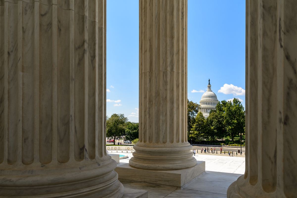 View between large fluted marble columns toward the U.S. Capitol dome under a blue sky