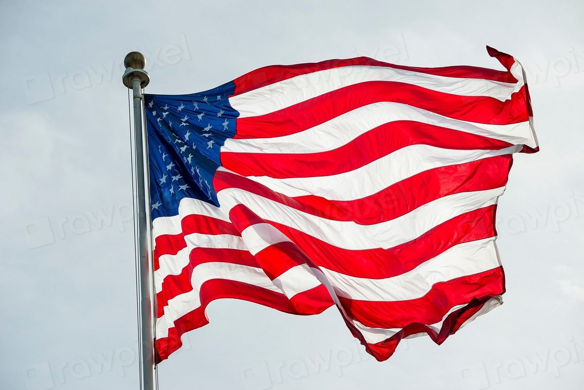 An American flag waves on a metal flagpole against a pale cloudy sky