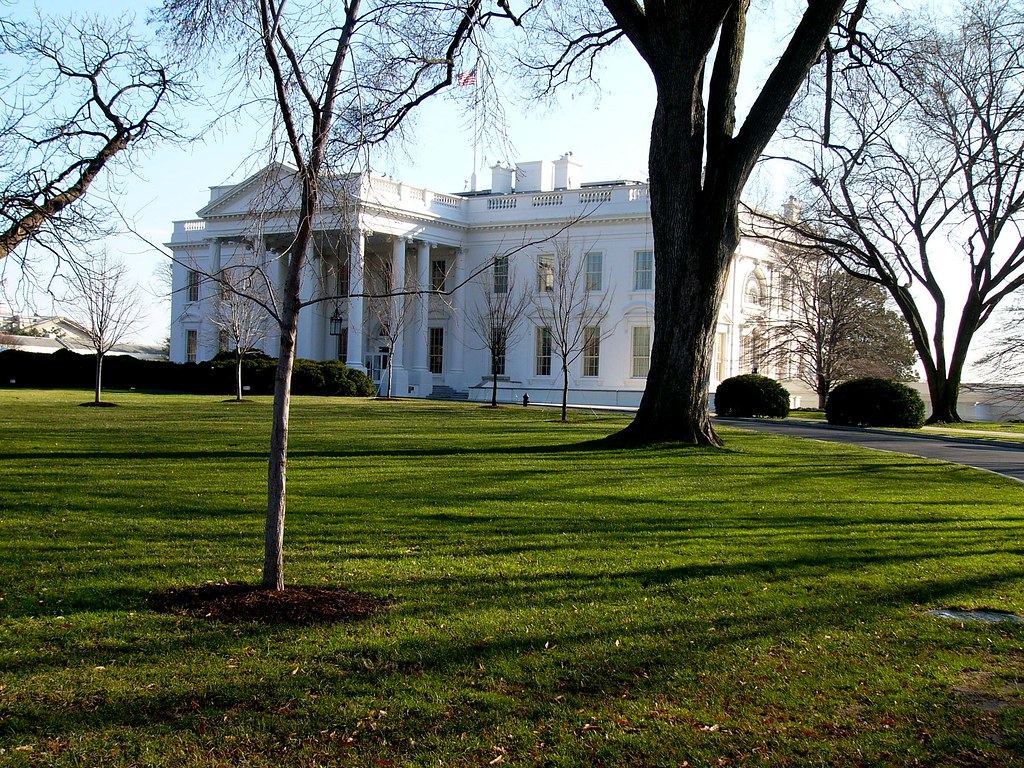 The north facade of the White House seen across a green lawn with bare winter trees
