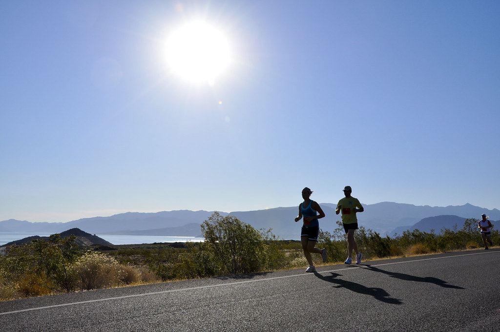 Runners on a sunny desert road with shrubs, a blue lake and mountains in the distance