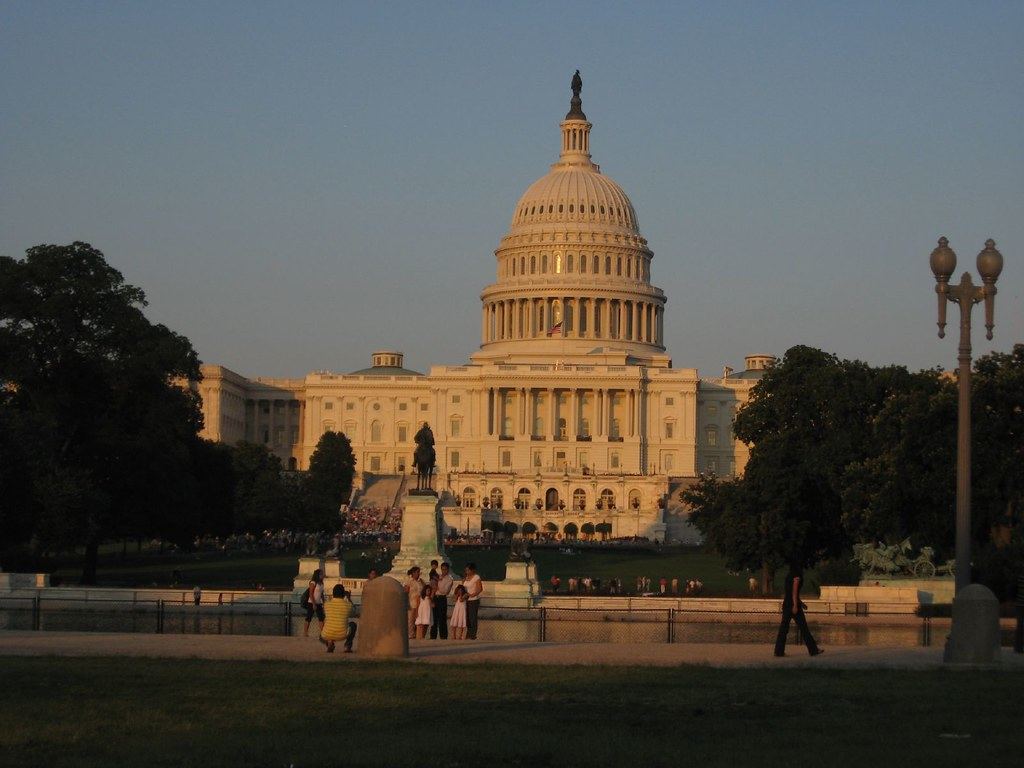 The U.S. Capitol dome in evening light, with trees, a statue and small groups of people on the lawn in front
