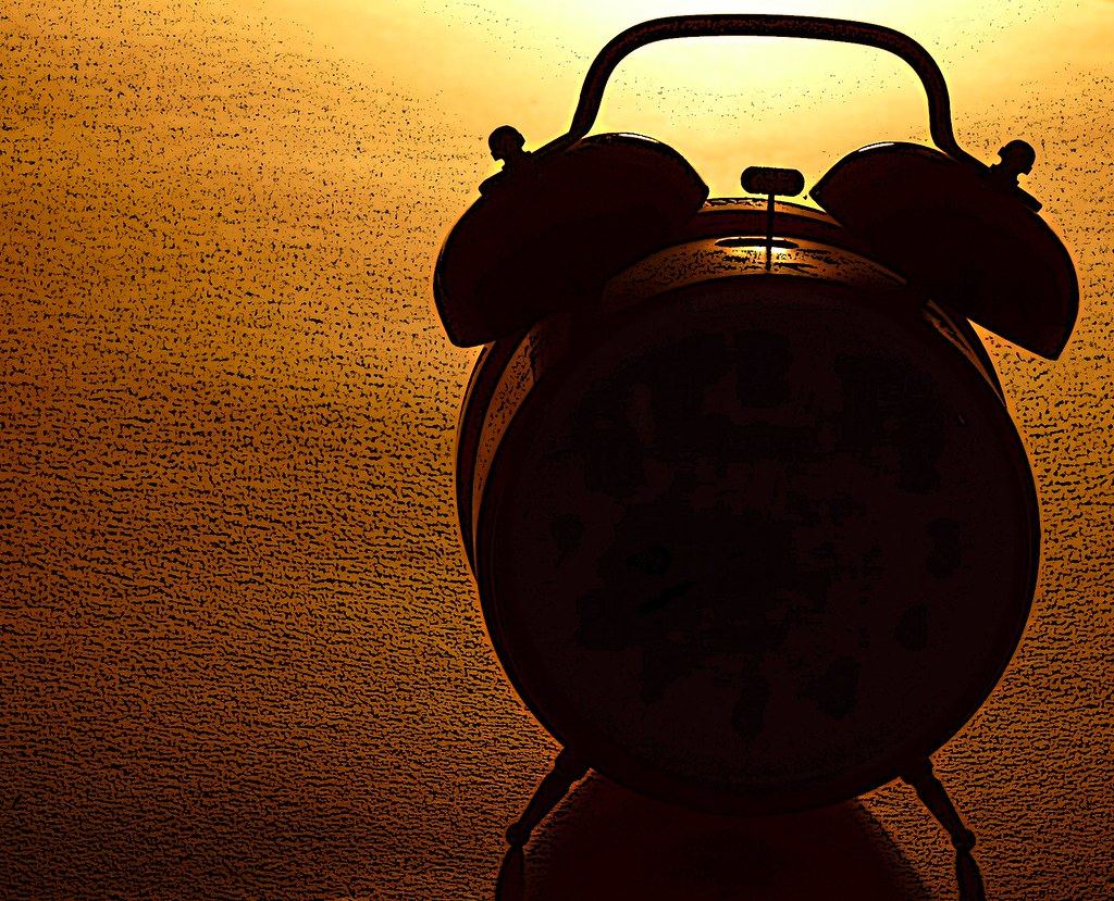 Silhouette of a twin-bell alarm clock against a warm orange, textured background