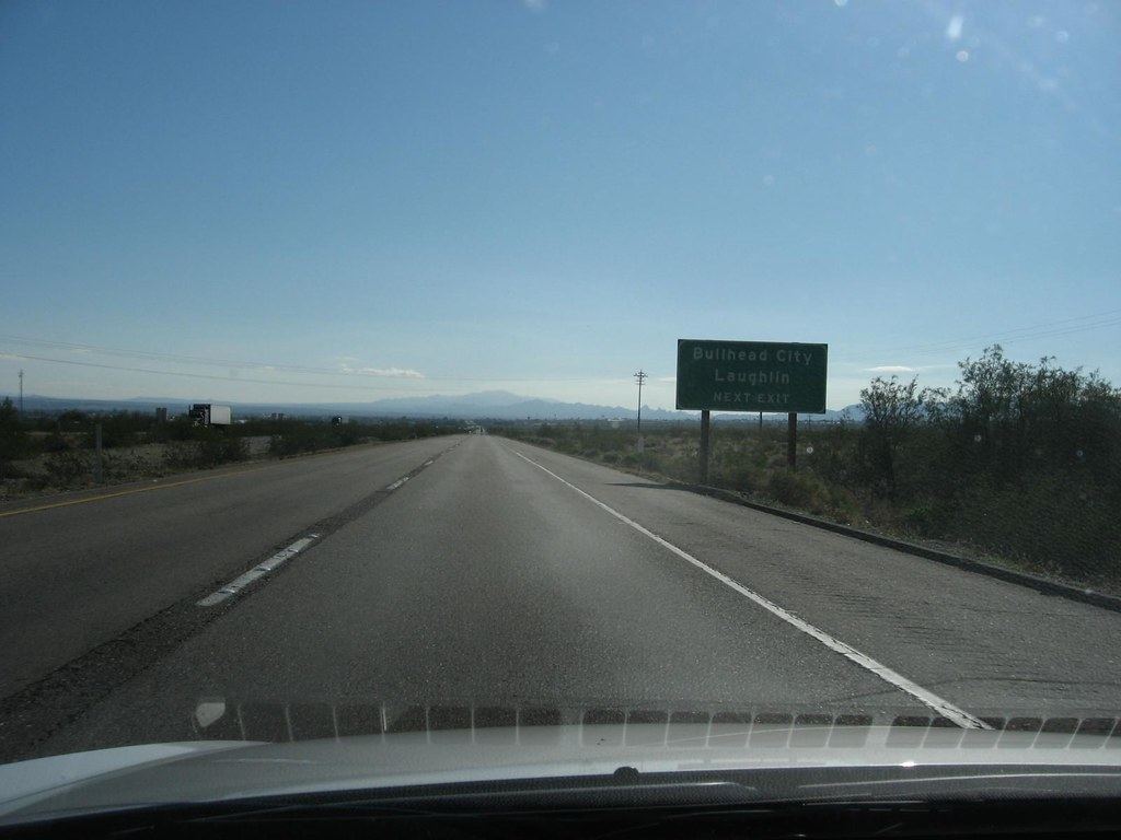 Desert highway through a car windshield with a green sign reading Bullhead City Laughlin Next Exit
