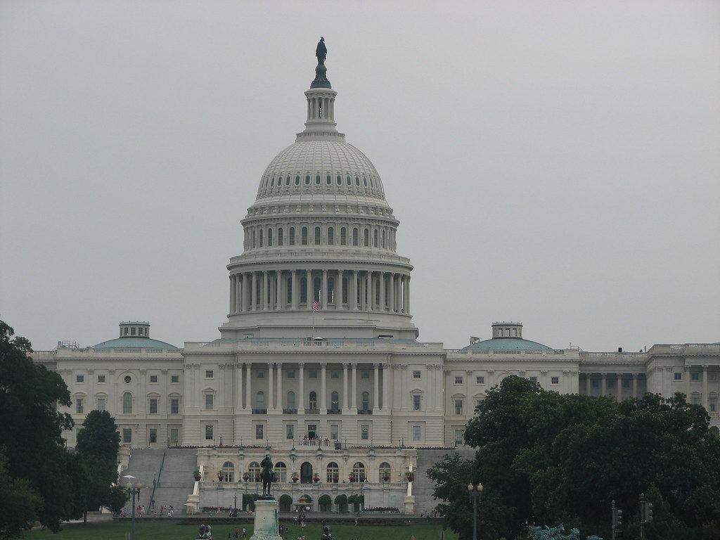 The US Capitol dome and west front under an overcast sky, with trees and a statue in the foreground