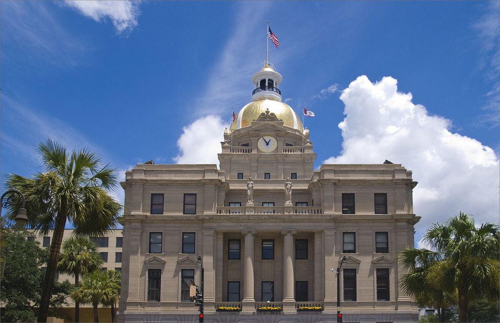 Stone government building with a gold dome, clock and American flag on top, framed by palm trees under a blue sky