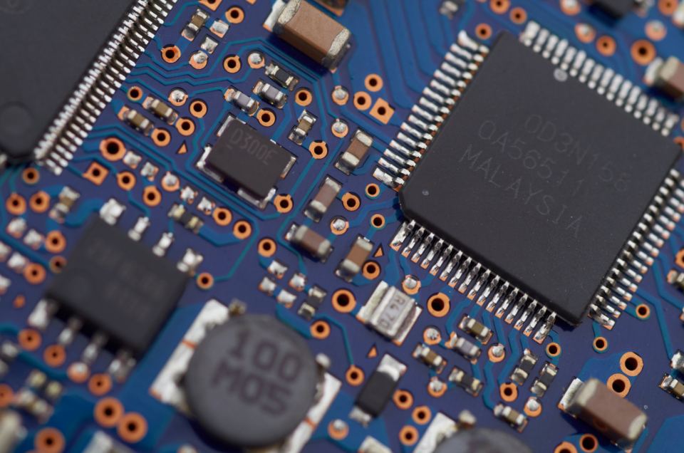 Close-up of a blue circuit board with a large black microchip, small components and copper solder pads