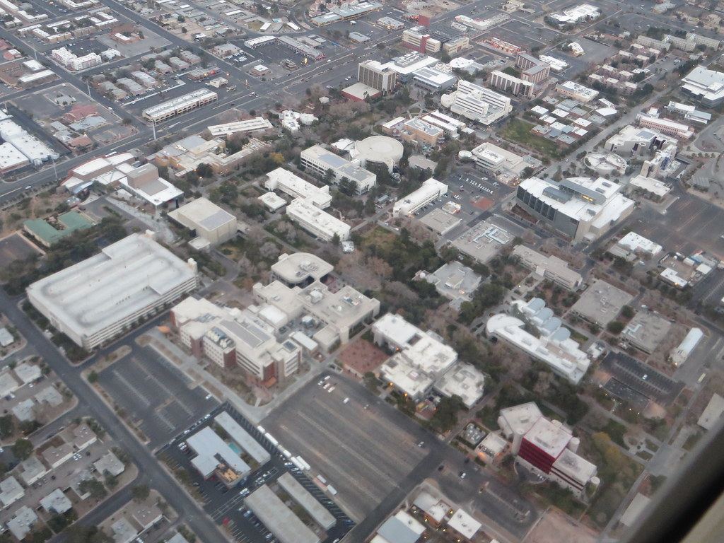 Aerial view of a university campus with low white buildings, trees, parking lots and surrounding city streets