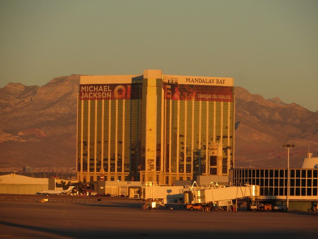 Gold-glass Mandalay Bay hotel tower at sunset, with mountains behind and airport jet bridges in front