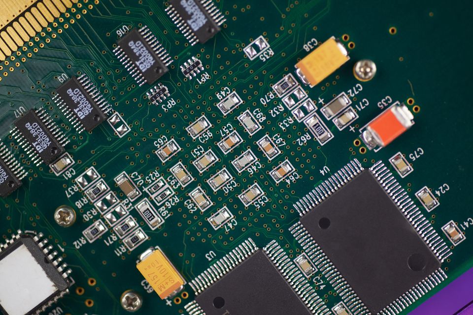 Close-up of a green circuit board with black microchips, small capacitors and orange and yellow components